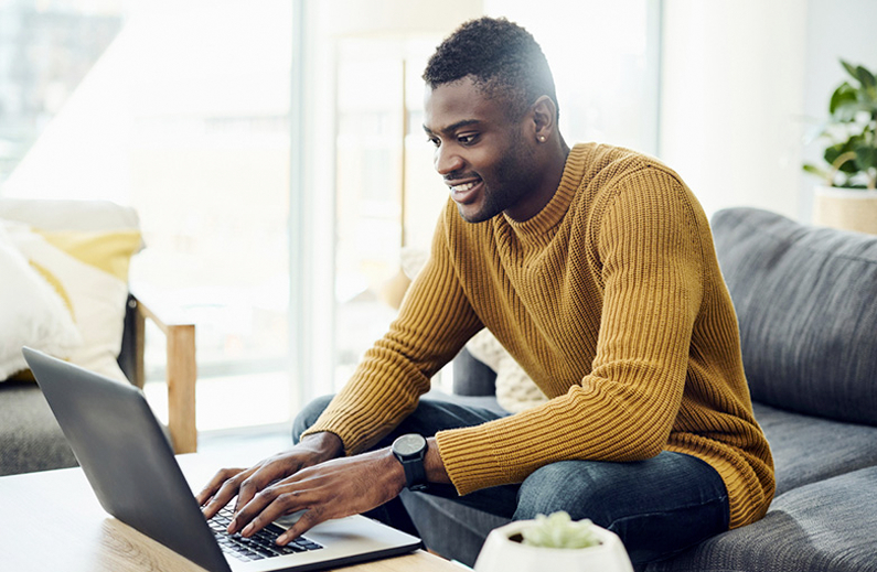 Black man in yellow sweater smiling at his laptop
